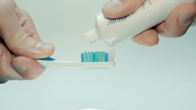 A man squeezes toothpaste from a tube onto a blue toothbrush on a white background. Closeup. The camera moves around. Slow mo, slo mo, slow motion, high speed camera