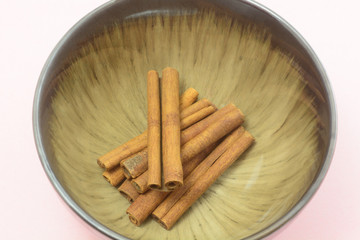 Closeup of cinnamon spice sticks in brown bowl on pink background
