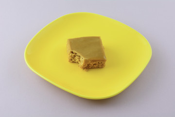 Toffee flapjack square cake bar with bite missing on yellow plate on lavender background