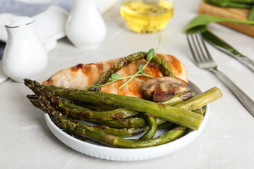 Tasty grilled chicken fillet served with asparagus on light grey marble table