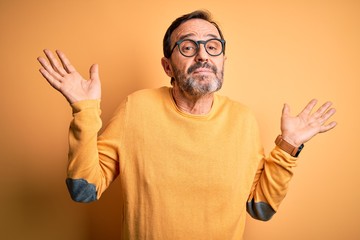Middle age hoary man wearing casual sweater and glasses over isolated yellow background clueless...