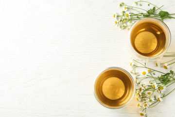 Flat lay composition with tea and chamomile flowers on white wooden table. Space for text