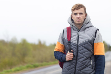 tired young man traveler with backpack trying to stop, catch taxi car, cab. guy stands near the road. concept of hitchhiking, Travel, journey.