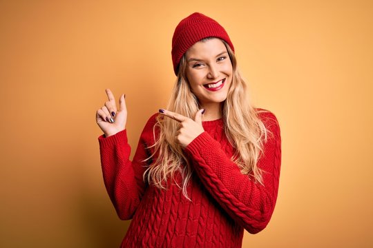 Young beautiful blonde woman wearing casual sweater and wool cap over white background smiling and looking at the camera pointing with two hands and fingers to the side.