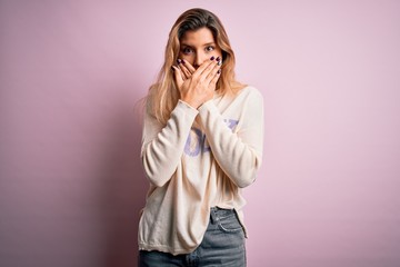 Young beautiful blonde woman wearing casual sweater standing over pink background shocked covering mouth with hands for mistake. Secret concept.