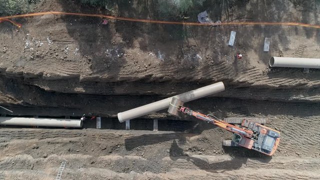 Aerial view of orange or red excavator tractor digging the sand ground to laying water pipeline installation in national infrastructure system. Outdoor construction workplace project