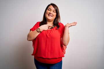 Beautiful brunette plus size woman wearing casual red t-shirt over isolated white background amazed and smiling to the camera while presenting with hand and pointing with finger.