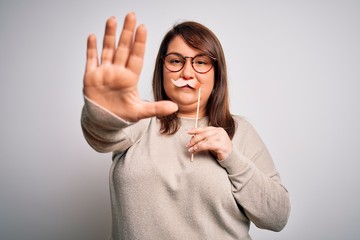 Beautiful plus size woman holding fake party mustache over isolated background with open hand doing...