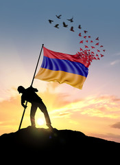 Armenia flag turn to birds while being planted by a man on a hill during sunrise.
