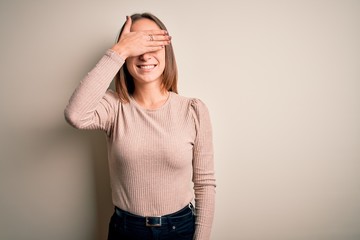 Young beautiful woman wearing casual sweater standing over isolated white background smiling and laughing with hand on face covering eyes for surprise. Blind concept.