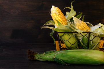 Fresh corn in a basket on a wooden table, closeup.