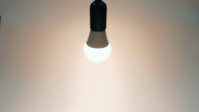 Energy-saving, eco-friendly Led bulb lamp lights on, swaying on the wire on a light background. Closeup. Slow mo, slo mo, slow motion, high speed camera