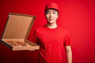 Young handsome chinese delivery man holding deliver box with delicious Italian pizza with a confident expression on smart face thinking serious