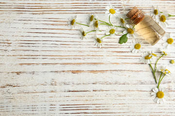 Bottle of essential oil and chamomiles on white wooden table, flat lay. Space for text