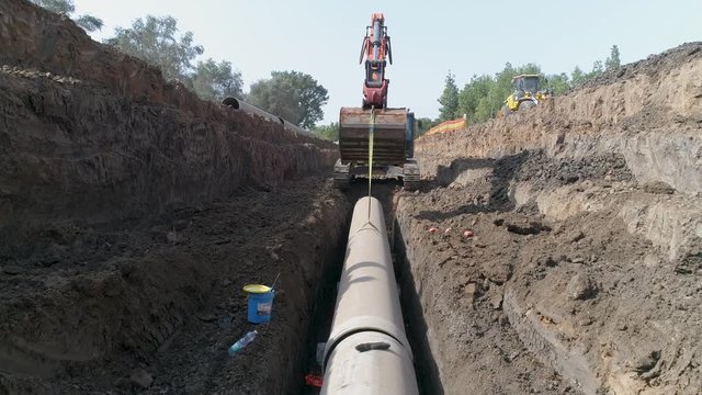 Aerial view of orange or red excavator tractor digging the sand ground to laying water pipeline installation in national infrastructure system. Outdoor construction workplace project