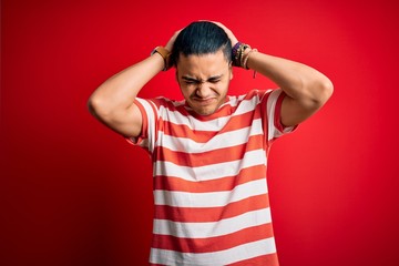 Fototapeta premium Young brazilian man wearing casual striped t-shirt standing over isolated red background suffering from headache desperate and stressed because pain and migraine. Hands on head.