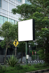 Square billboard with a backdrop of trees and buildings. Nameplate with short post. blank billboard, signboard mockup. The billboard is in the middle of a very strategic highway.