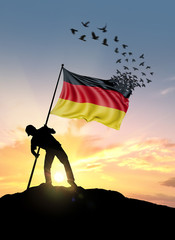 Germany flag turn to birds while being planted by a man on a hill during sunrise.