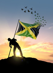 Jamaica flag turn to birds while being planted by a man on a hill during sunrise.