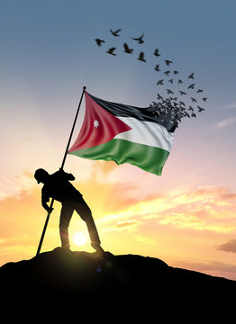 Jordan flag turn to birds while being planted by a man on a hill during sunrise.