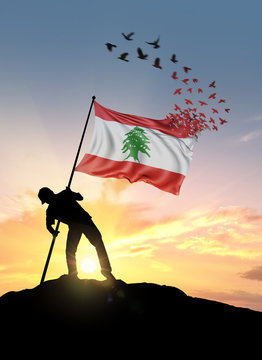Lebanon flag turn to birds while being planted by a man on a hill during sunrise.