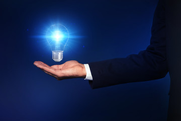 Idea concept. Businessman with glowing light bulb on dark background, closeup