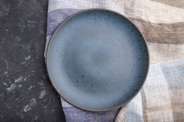 Empty blue ceramic plate on black concrete background. Top view, close up.