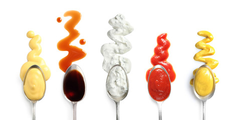 Set of spoons with different delicious sauces on white background, top view