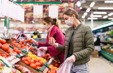 Social distancing in a supermarket. A young woman in a disposable face mask buying fruits and vegetables and putting them in a grocery basket. Shopping during the Coronavirus Covid-19 epidemic 2020