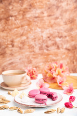 Purple macarons or macaroons cakes with cup of coffee on a white and brown concrete background. Side view, copy space, selective focus.