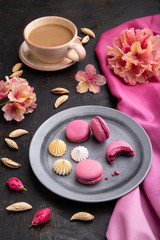 Purple macarons or macaroons cakes with cup of coffee on a black concrete background. Side view, close up.