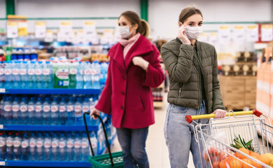 Social distancing in a supermarket. A young women in a disposable face masks and gloves with grocery basket. Shopping during the Coronavirus Covid-19 epidemic 2020
