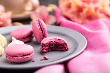 Purple macarons or macaroons cakes with cup of coffee on a black concrete background. Side view, selective focus.