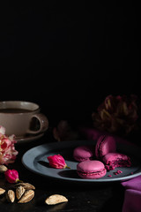 Purple macarons or macaroons cakes with cup of coffee on a black concrete background. Hard light, low key. Side view, copy space.