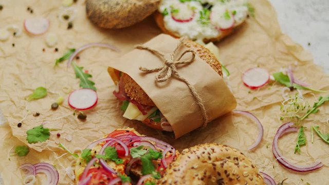 Bagels with ham, cream cheese, hummus, radish wrapped in brown baking paper ready for take away