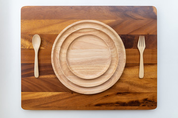 The lacquered round wooden plates are stacked on multiple layers. Beside, there are spoons and forks, as well as the backdrop of the acacia wood with beautiful wood patterns.