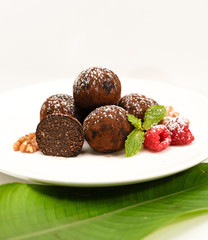 chocolate balls made from cocoa and walnuts with condensed milk, cakes on a white plate with raspberries on a banana leaf, homemade sweets on a white background