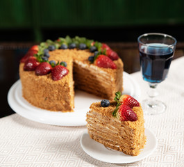square photo, a slice of cake on a plate, a large honey cake decorated with strawberries and blueberries, homemade pastries on a dish and a light napkin, Thai blue tea in a mug
