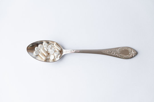 Medicine and health, treatment, pharmacy, coronavirus, pandemic, epidemic concept - layout one silver big tablespoon with different pills and capsules on a white background copy space.