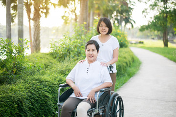 Caregiver take care to elderly asian woman sitting on wheelchair at public park,Senior care...