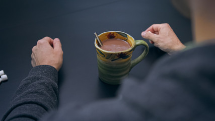 High quality close-up of a man mixing hot chocolate beverage in his cup with small white...