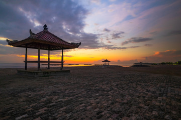 Sunrise seascape. Traditional balinese gazebos. Cloudy sky. Sunlight at horizon. Nusa Dua beach, Bali, Indonesia.