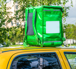 Closeup of green food delivery box, backpack standing on the top of yellow car. Mockup for food delivery service. Copy space.