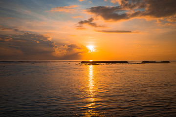 Rising sun at horizon. Sunrise seascape. Amazing water reflection. Cloudy sky. Sunlight at horizon. Nusa Dua beach, Bali, Indonesia.