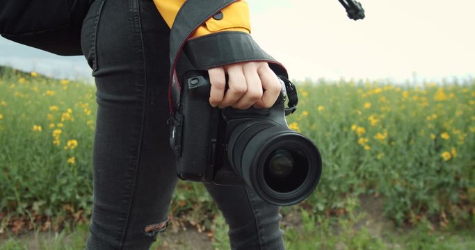 Close up of female photographer in casual outfit carrying on her camera while walking on green wheat field. Mature woman taking pictures of beautiful nature around.