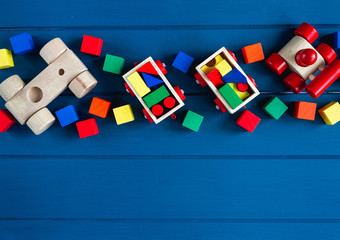 Multicolored wooden toys cubes, pyramid and cars on classic blue background. Set colorful toys for games in kindergarten, preschool kids. Close up, top view, copy space