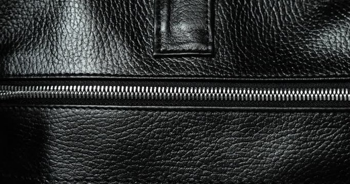 Man unzips metal zip testing it on a leather black bag, hand closeup view. Macro shot of unzipping metallic zipper on black leather accessory with guy's hand. Expensive brutal accessory.