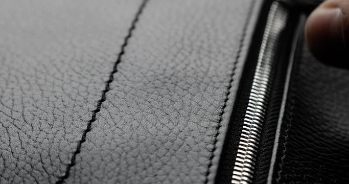 Testing metal zipper zips and unzips it on leather bag, man's hand closeup. Macro shot of unzipping and zipping metallic zipper on black leather accessory with guy's hand. Expensive brutal accessory.