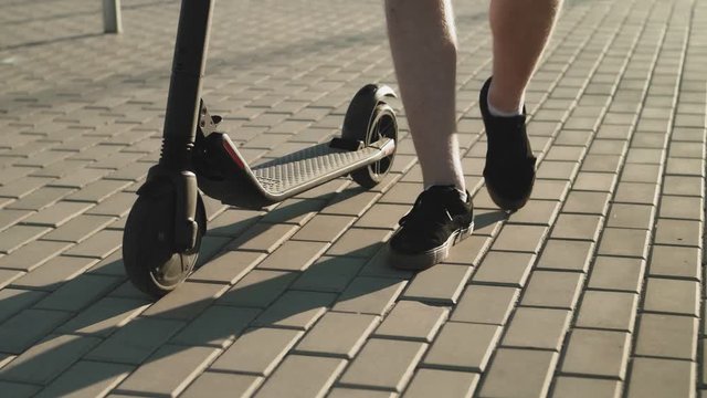 Attractive man in shorts and a blue shirt walking with his the electric kick scooter