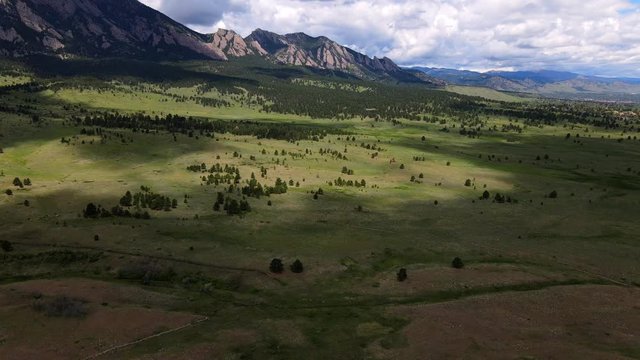 fly over green fields with flatiron mountains in the background colorado